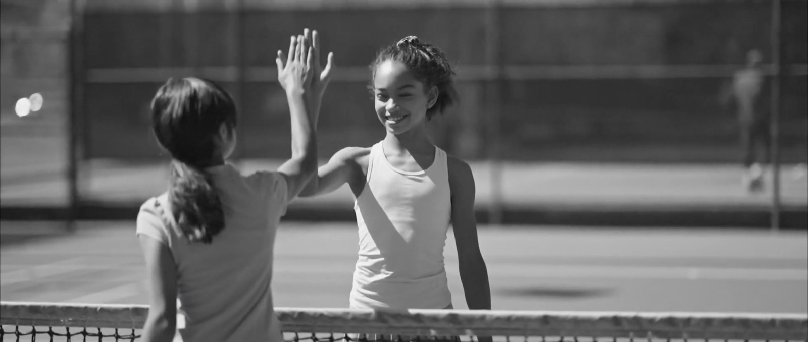 Dos jóvenes jugadoras de tenis celebran un punto chocando las manos.